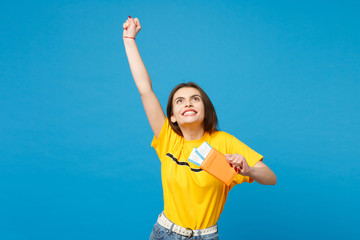 Happy young woman in vivid casual clothes looking up, doing winner gesture, holding passport...