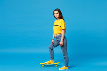 Side view of attractive young woman in vivid casual clothes looking camera, standing with yellow...