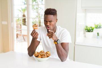 African american man eating chocolate chips muffin pointing with finger to the camera and to you, hand sign, positive and confident gesture from the front