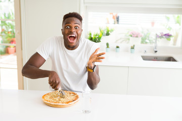 African american man eating cheese pizza at home very happy and excited, winner expression celebrating victory screaming with big smile and raised hands