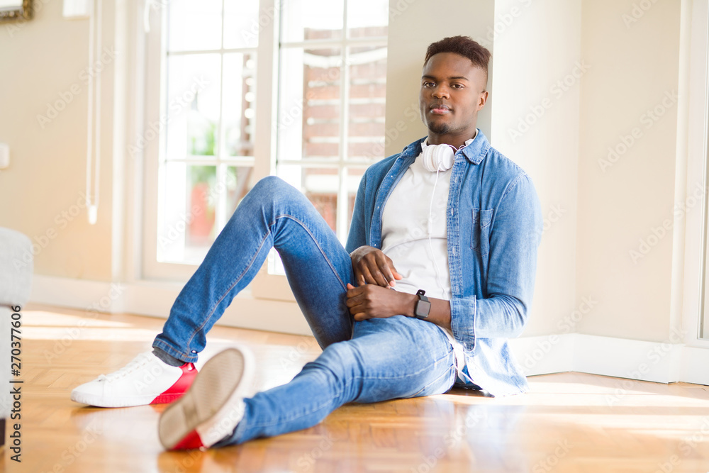 Poster african american man wearing headphones listening to music sitting on the floor with serious express