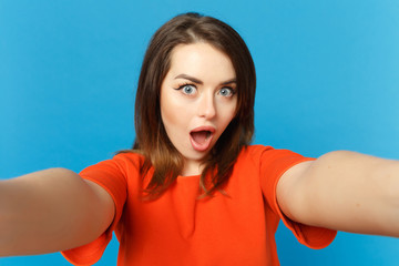 Close up photo of young woman in red orange clothes looking camera posing doing selfie shot isolated over trendy blue background, studio portrait. People lifestyle fashion concept. Mock up copy space.