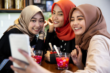 Veiled young women relaxing using smartphone for selfie while waiting breaking their fast in the afternoon