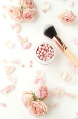 Makeup cosmetic accessories products  powder and powder brush, pink flowers roses on white background. Flat lay. Top view. 