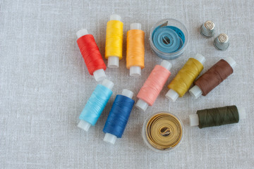 Fototapeta na wymiar coils of colored threads for sewing, centimeter tapes and thimbles on a light gray background, copy space