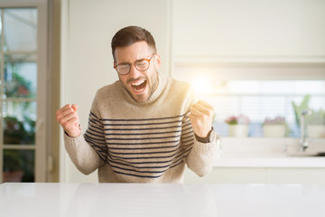 Young handsome man wearing glasses at home very happy and excited doing winner gesture with arms...