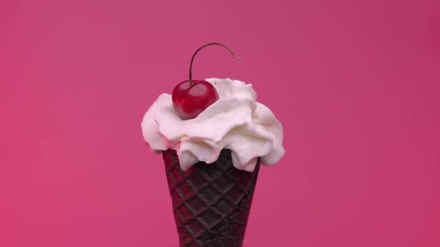 Soft ice cream in black cone with cherry against pink background