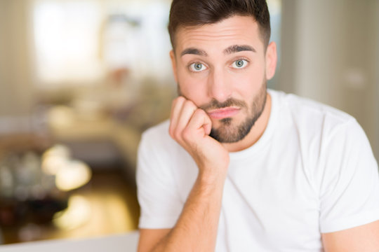 Young handsome man wearing casual white t-shirt at home thinking looking tired and bored with depression problems with crossed arms.