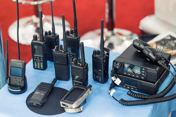 Many portable radio transceivers on table at technology exhibition. Different walkie-talkie radio set. Communication devices choice for military and civil use © Kirill Gorlov