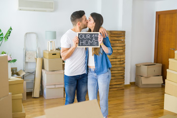 Fototapeta na wymiar Beautiful young couple moving to a new house, smiling very happy holding blackboard with our first home text