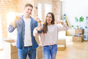 Beautiful young couple moving to a new house looking confident with smile on face, pointing oneself...