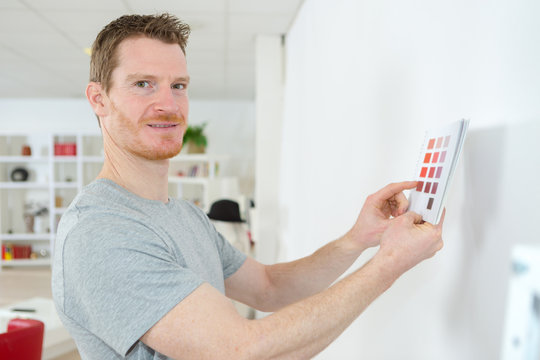 man holding paint color samples up to wall