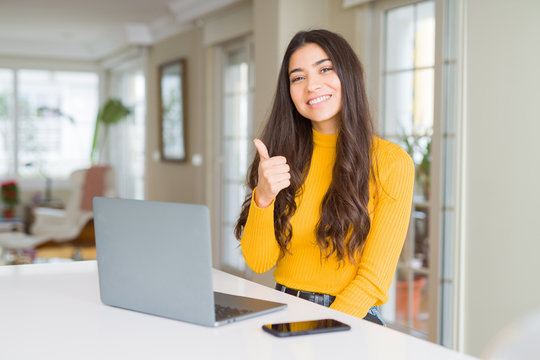 Young woman using computer laptop doing happy thumbs up gesture with hand. Approving expression looking at the camera with showing success.