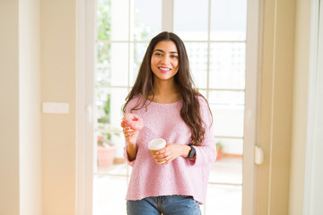 Young worker woman taking a break eating tasty pink donut and drinking a cup of coffee