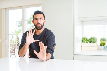 Fototapeta premium Handsome hispanic man wearing casual sweater at home afraid and terrified with fear expression stop gesture with hands, shouting in shock. Panic concept.