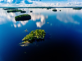 Aerial view small island in blue lake landscape with green forests on a sunny summer day in Finland.