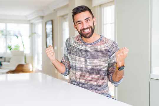 Handsome hispanic man wearing casual sweater at home celebrating surprised and amazed for success with arms raised and open eyes. Winner concept.
