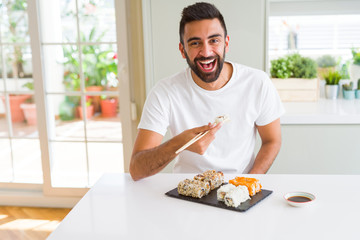 Handsome man smiling happy enjoying eating fresh colorful asian sushi using chopsticks