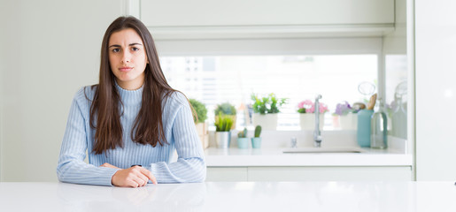 Wide angle picture of beautiful young woman sitting on white table at home skeptic and nervous, frowning upset because of problem. Negative person.