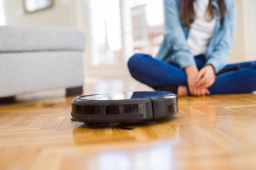 Young woman using automatic vacuum cleaner to clean the floor, controling machine housework robot