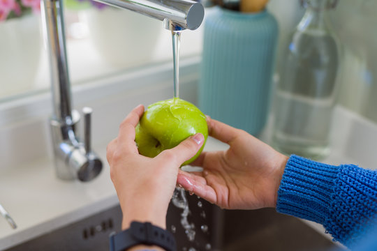 Young woman washing vegetables and fruit using water from sink