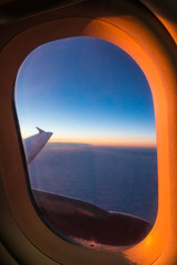 The wing of the airplane above a clouds, view from the porthole beautifully illuminated by the setting sun