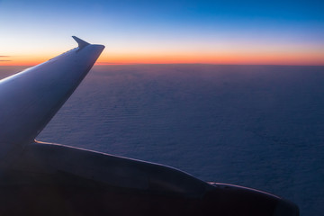 Obraz na płótnie Canvas The wing of the airplane above the clouds closeup at sunset, view from the porthole