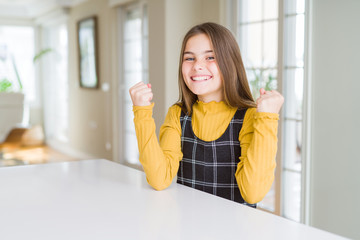 Fototapeta premium Beautiful young girl kid sitting on the table celebrating surprised and amazed for success with arms raised and open eyes. Winner concept.