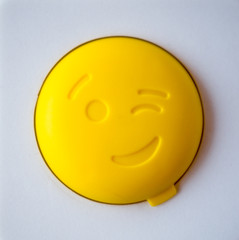 Yellow PET bottle cap with a smiley face on a white background. Plastic waste concept.