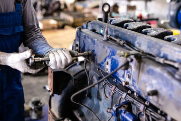 Fototapeta premium Mechanic repairs old motor of truck in a car repair station. Disassemble engine block vehicle. Motor capital repair. Car service concept