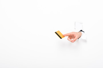 partial view of man holding Credit card from hole in wall on white with copy space