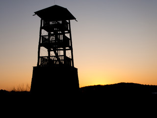 Wooden watchtower silhouette before sunrise. Hunters' outlook with a stone base in the morning.