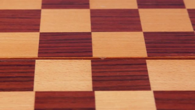 Malachite checker and marble checker on a wooden checkerboard. Close-up