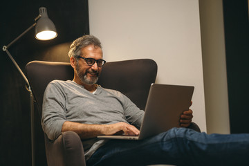 middle aged man using laptop relaxed in sofa in his home