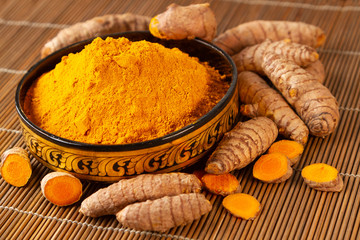 turmeric powder and turmeric roots in closeup selective focus on turmeric powder