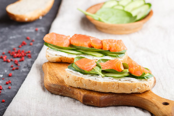 Smoked salmon sandwiches with cucumber and spinach on wooden board on a linen background.