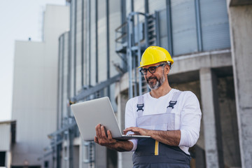 worker using laptop, grain silo in blurred background