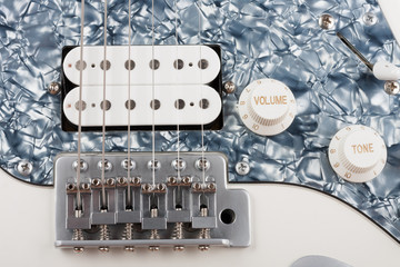 Close up of bridge and  humbucker and controls on white white electric guitar, studio shoot. © patrikslezak