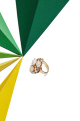 Shot of massive cocktail ring with snow-white floral application and rhinestones. The accessory is isolated against the snowy background near multicolored 3-dimensional triangles of different size.