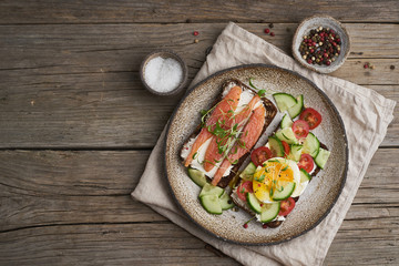 Fototapeta na wymiar Smorrebrod - traditional Danish sandwiches. Black rye bread with salmon, cream cheese, cucumber, tomatoes on wooden table, copy space, top view.