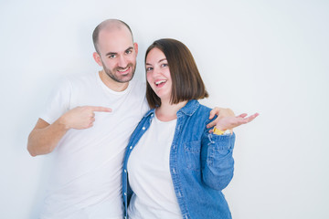 Young couple together over white isolated background amazed and smiling to the camera while presenting with hand and pointing with finger.