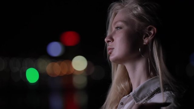 Face profile beautiful blonde woman touch her long hair in night city, slow motion