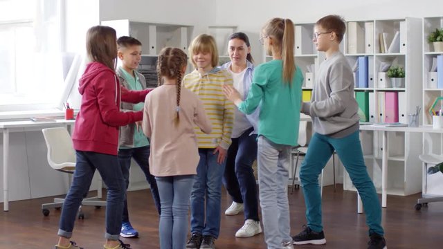 Full shot of six young teenagers playing trust game with mental health coach at her sunlit office, standing together in circle, with one boy in middle falling with closed eyes and others catching himF