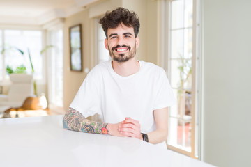 Young man wearing casual t-shirt sitting on white table with a happy and cool smile on face. Lucky person.