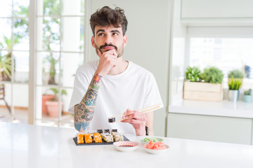 Young man eating asian sushi from home delivery serious face thinking about question, very confused idea