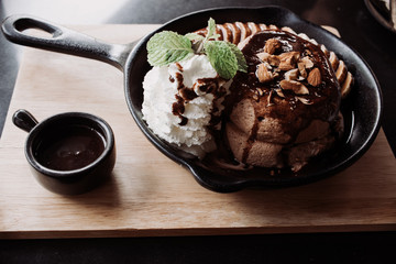 Delicious pancake with banana chocolate and vanilla ice cream on black iron pan over cock coaster.