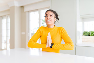 Beautiful african american woman with afro hair wearing a casual yellow sweater begging and praying with hands together with hope expression on face very emotional and worried. Asking for forgiveness