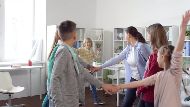 Rear shot of blond 12-year-old boy running through human corridor made by other kids and teacher standing in pairs and holding hands, lifting them to let him pass, during after school group counseling