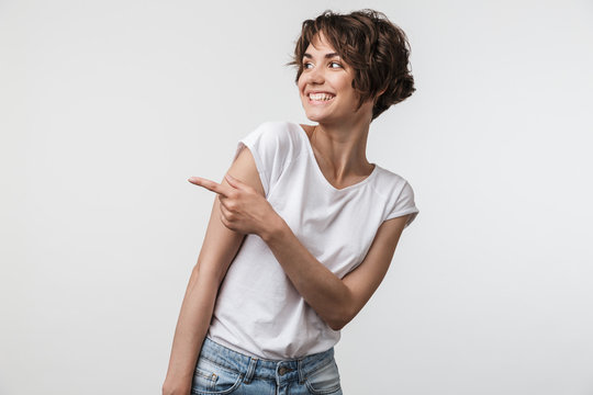 Portrait of happy woman with short hair in basic t-shirt rejoicing and pointing finger at copyspace