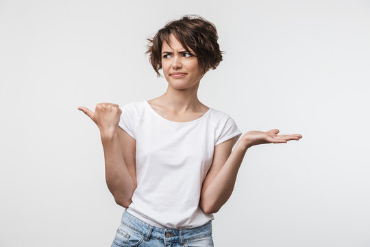 Image of confused woman with short hair in basic t-shirt pointing finger aside at copyspace